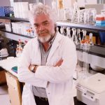 Dr. Frank Plummer poses for the photo in a lab. He is wearing a white coat.