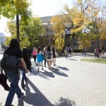 People walking on brick sidewalk with autumn trees in the background.