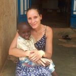 Lindsay Aboud is seated, holding a village boy on her lap in Uganda.