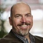 Man with shaved head and salt and pepper short beard and moustache