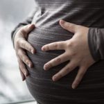 Closeup of a pregnant woman's belly, with both hands on belly.