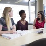 Three people sit around a table working on resumes