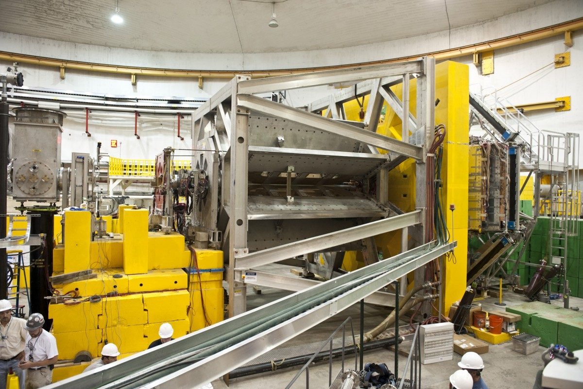 A partial view of the apparatus used at Jefferson Lab to measure the weak charge of the proton. The electron beam travelled down a vacuum pipe from left to right. Electrons scattered from the liquid hydrogen target were selected by a contoured shielding system and deflected radially outwards by an 8-fold symmetric magnetic spectrometer in the center of the figure; they were detected by an array of quartz Cerenkov bars forming the black octagonal structure at the far right. The Canadian group designed and constructed the magnetic field coils with support from NSERC and TRIUMF. U of M students and scientists played a key role in building and operating the electron detector array, which was surrounded by a heavy concrete shielding structure (not shown) during data taking.