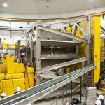 A partial view of the apparatus used at Jefferson Lab to measure the weak charge of the proton. The electron beam travelled down a vacuum pipe from left to right. Electrons scattered from the liquid hydrogen target were selected by a contoured shielding system and deflected radially outwards by an 8-fold symmetric magnetic spectrometer in the center of the figure; they were detected by an array of quartz Cerenkov bars forming the black octagonal structure at the far right. The Canadian group designed and constructed the magnetic field coils with support from NSERC and TRIUMF. U of M students and scientists played a key role in building and operating the electron detector array, which was surrounded by a heavy concrete shielding structure (not shown) during data taking.