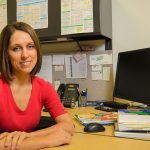 Meghan Azad, UM researcher in pediatric health sits in an office at a desk next to a computer.