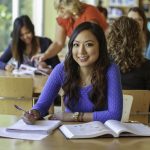 Smiling student sits at a library table studying.