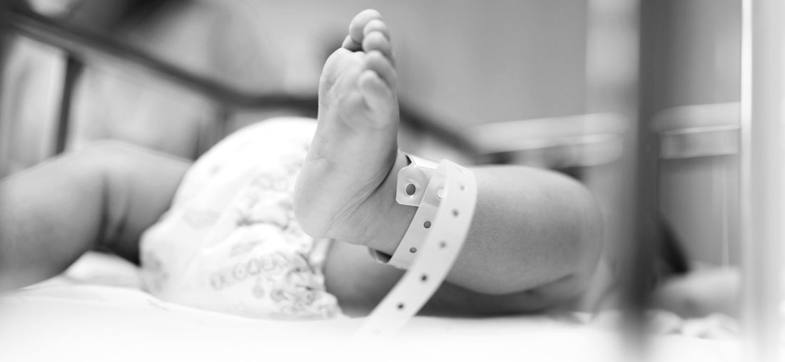 black and white photo of a baby in the hospital with an id bracelet on their ankle.
