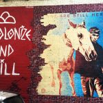 A mural featuring the wordsDecolonize and Chill - We are Still Here, and a man walking a horse