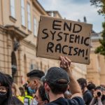 A protestor holds a sign that reads End Systemic Racism