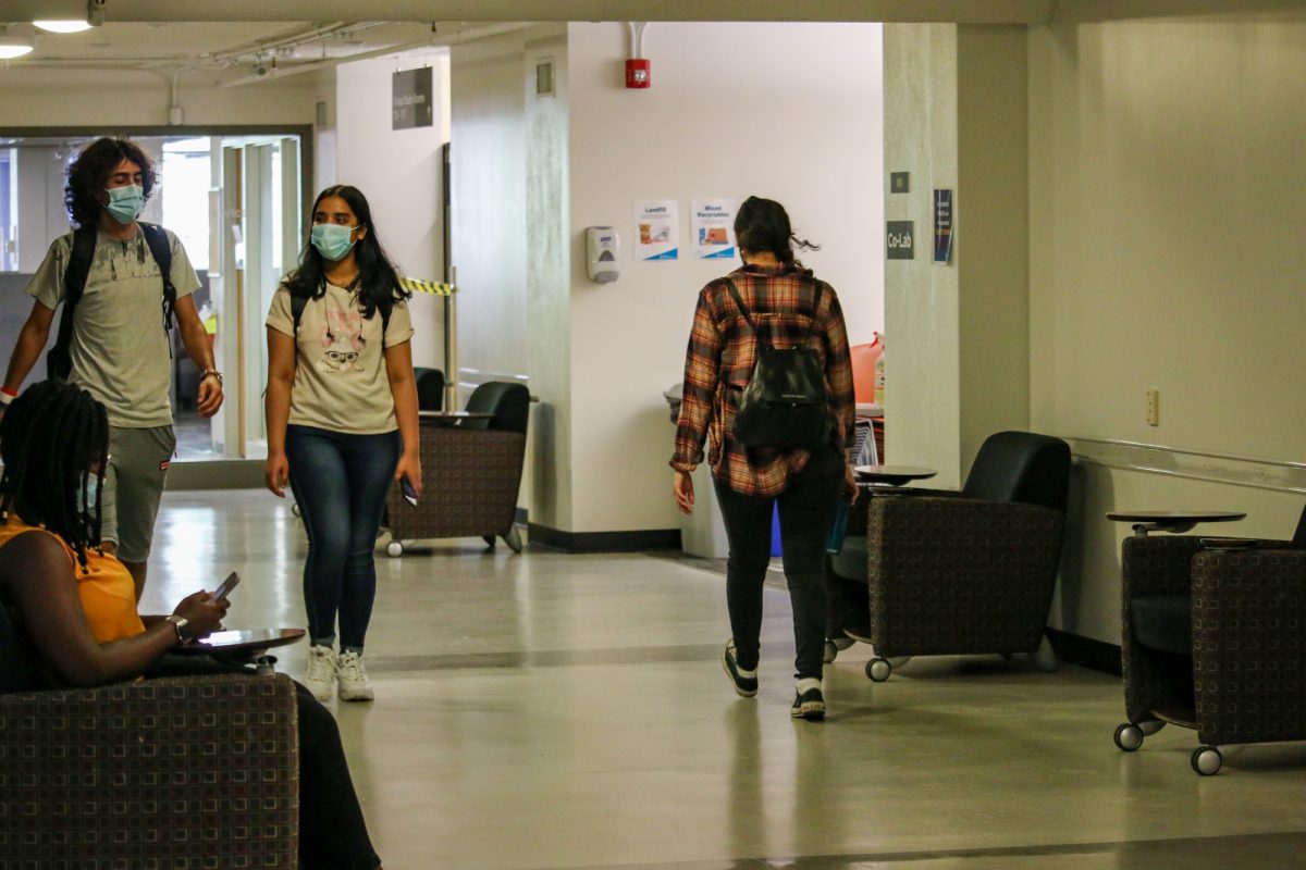 Two students wearing masks walk together down a hallway on campus.
