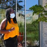 Student wearing mask outdoors on campus with leafy background