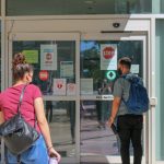 Two people wearing masks are approaching an entrance to Bannatyne campus.