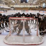 women's hockey team huddled around the net on the ice.