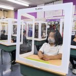 Elementary school students at their desks behind barriers for COVID-19