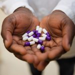 The cupped hands of a person wearing a white lab coat hold medication capsules.