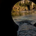 Water flows from a metal pipe into a river.