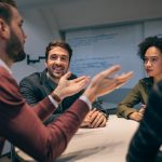 Four individuals sitting around a small table in a classroom, collaborating on a discussion.