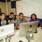 Group of students huddled around two computers.