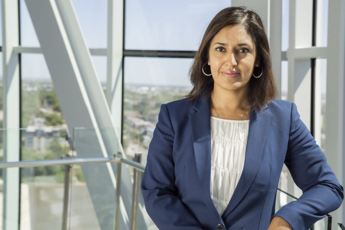 Woman in professional clothing stands in front of bank of windows with the Winnipeg cityscape in view behind her.