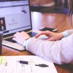 Person types on laptop computer, with a phone and mug nearby.