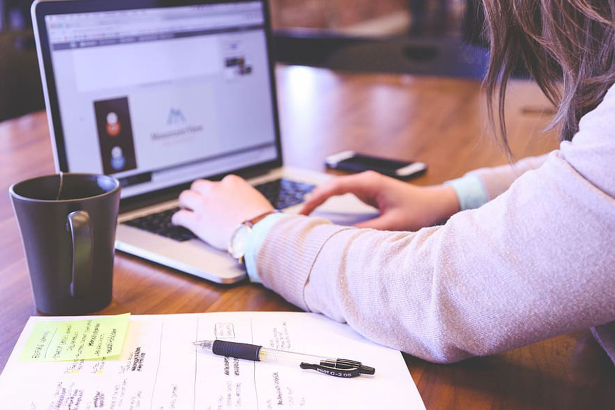 Person types on laptop computer, with a phone and mug nearby.
