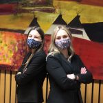 Two law students wearing face masks standing back to back.
