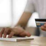 someone typing on a computer with their credit card in their hand