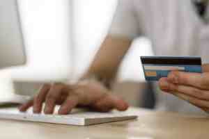 someone typing on a computer with their credit card in their hand