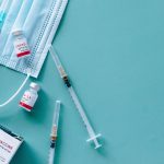 COVID-19 vaccine vials, syringes and a blue mask on a green table.
