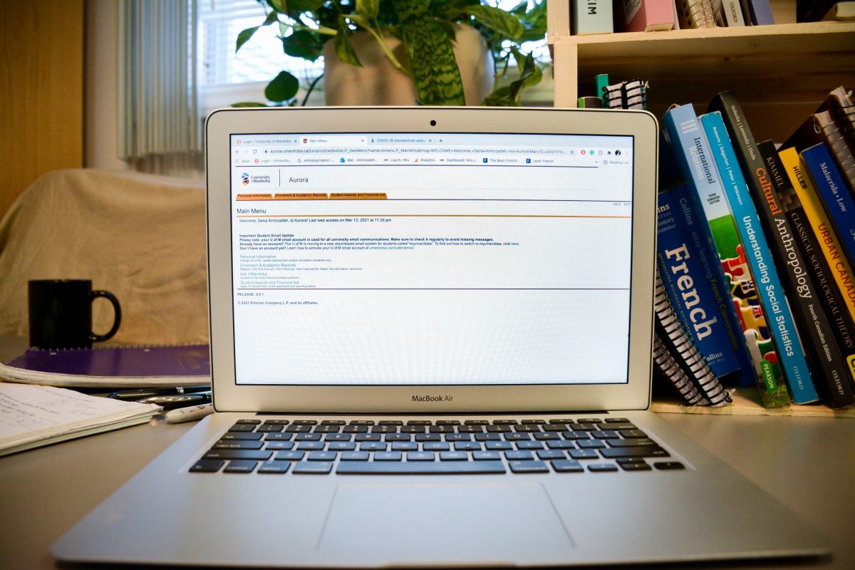 A computer sits on a desk with Aurora on the screen. In the background there is a collection of books from a variety of University classes.