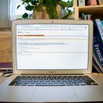 A computer sits on a desk with Aurora on the screen. In the background there is a collection of books from a variety of University classes.