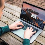 student in sweatshirt working on a laptop at a picnic bench