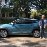 Dr. Nazim Cicek stands outside alongside his full electric vehicle, under a large tree on a sunny day.