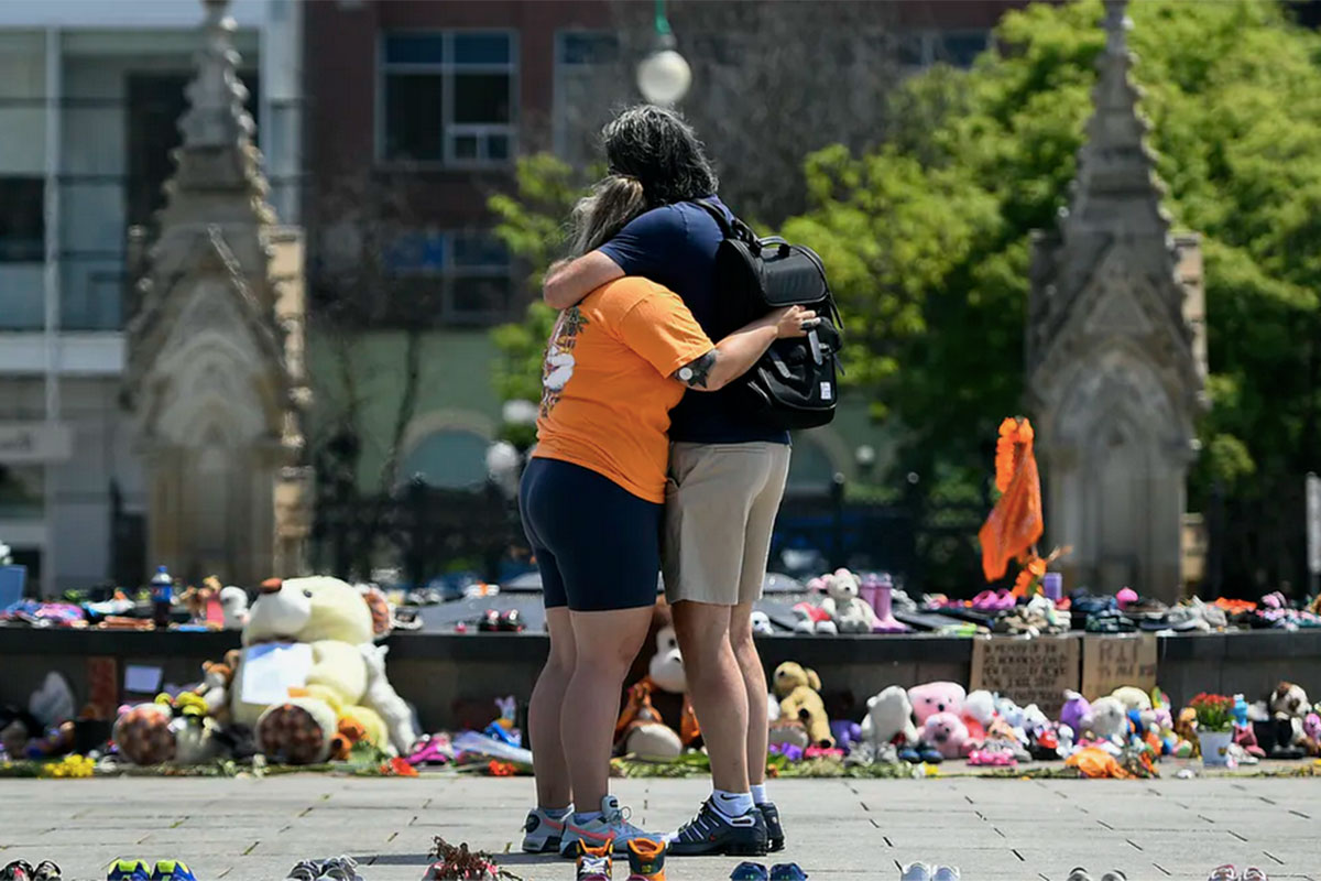 People embrace in front of the Centennial Flame on Parliament Hill at a memorial for the 215 children whose remains were found at the grounds of the former Kamloops Indian Residential School. // THE CANADIAN PRESS/Justin Tang