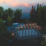 An aerial photo of a building being constructed on treed land near a lake.