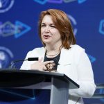 Woman speaking at podium with hand placed over her heart.