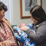 A woman holds a baby as another woman looks on.