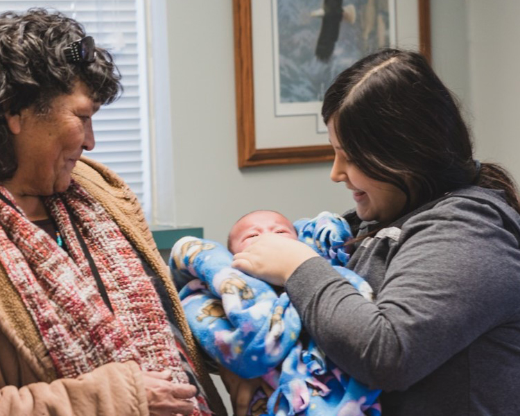 A woman holds a baby as another woman looks on.