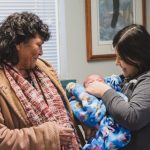 A woman holds a baby while another woman looks on.