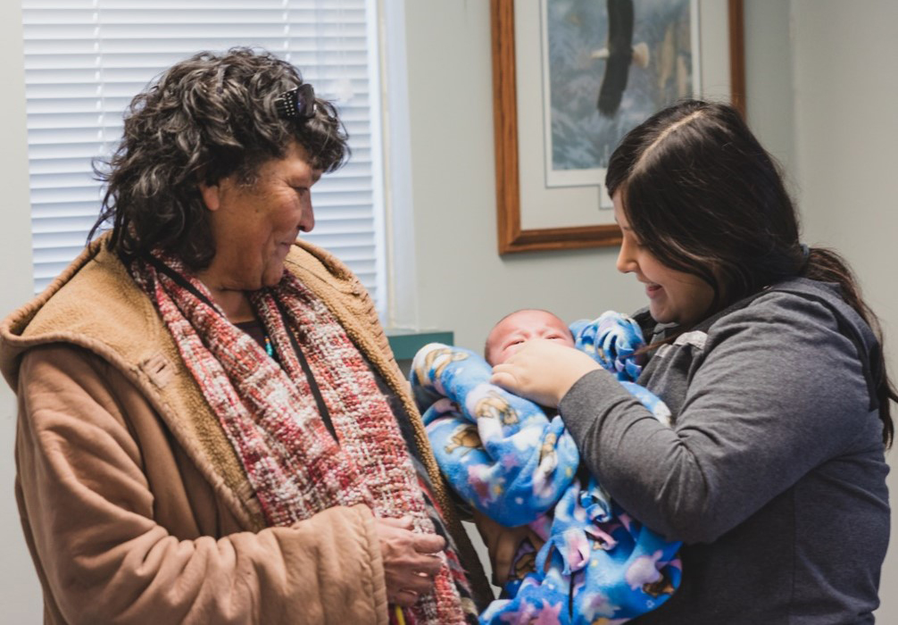 A woman holds a baby while another woman looks on.