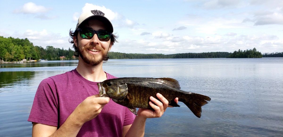 Phil Grayson, holding a fish with a lake in the background