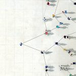 An overhead view of people standing in a crowd, all connected by interlinked strings.