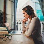Woman by a window contemplates the future as she gazes into her laptop