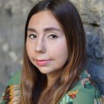 close-up of woman leaning against brick wall looking into the camera