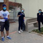 Three students stand outside. One student holds up a filled garbage bag.