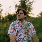 Justin Lagan stands in a field at sunset in a bright floral shirt.
