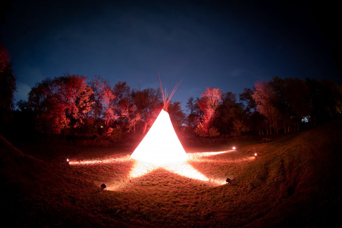 teepee bathed in orange spotlights with a night sky