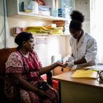 At a clinic in Nairobi, Kenya, a nurse or doctor examines the hand of a seated patient.