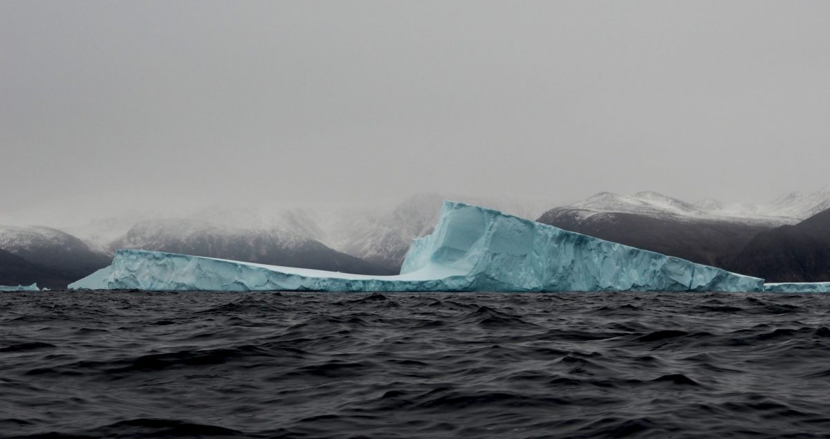 an iceberg in open water with hazy clouds surrounding it