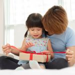 A mother helps a child open a gift.